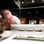 Kevin Kubo, 32, junior of Chadron, peers into a glass display case holding two miniature train models Wednesday afternoon in Memorial Hall’s main gallery. —Photo by T.J. Thomson